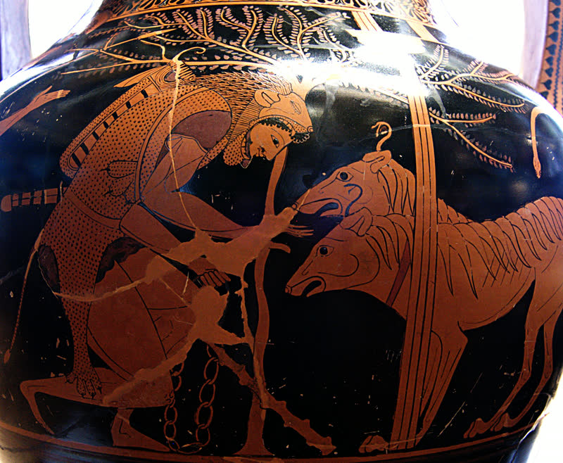 Héracles, de pele de leão sobre a cabeça, estende a mão para Cérbero e o prende pela corrente; o cão do Hades traz duas cabeças e serpentes saindo do corpo. Lado A, de figuras vermelhas, de uma ânfora ática bilíngue do Pintor de Andócides, ca. 530–520 a.C. Musée du Louvre, Paris (F 204).