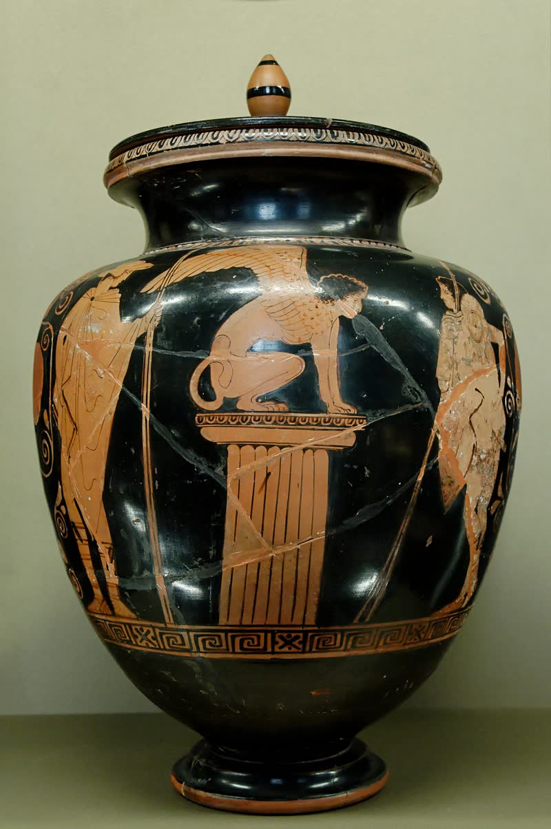 A Esfinge, de asas fechadas, agachada no alto de uma coluna jônica; Édipo à direita, de pétaso e lança, e Hermes à esquerda. Estâmnos ático de figuras vermelhas, ca. 440 a.C., atribuído ao Pintor de Menelau. Musée du Louvre, Paris (G 417).