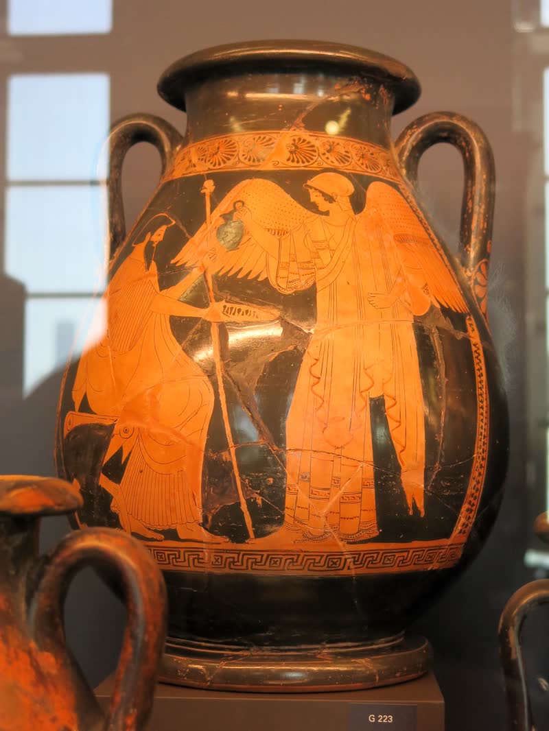 Íris, de asas abertas e cetro na mão, serve a libação a Zeus sentado no trono. Pélice ática de figuras vermelhas, ca. 480–470 a.C.; achada na Itália central. Musée du Louvre, Paris (G 223 / Cp 699).