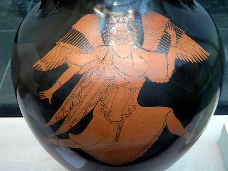 Medusa corre de asas abertas, fugindo de Perseu: o rosto redondo tem presas, a língua para fora, os olhos arregalados e um anel de serpentes em volta da cabeça. Detalhe de uma ânfora ática de figuras vermelhas, ca. 490 a.C., atribuída ao Pintor de Berlim. Staatliche Antikensammlungen, Munique.