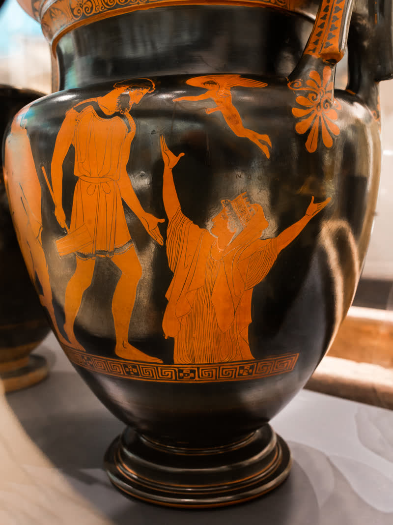Zeus de cetro e Hermes assistem enquanto Epimeteu, de malho na mão, recebe Pandora, que sobe da terra de braços erguidos e coroa na cabeça; Eros voa acima com uma fita. Os nomes estão pintados ao lado das figuras. Lado A de uma cratera de volutas ática de figuras vermelhas, ca. 450 a.C. Ashmolean Museum, Oxford (V 525 / G 275).