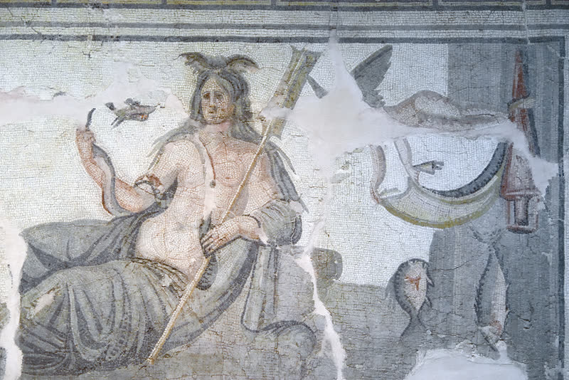 Tétis reclinada, as pinças de caranguejo erguidas sobre a testa e o remo apoiado no ombro; na mão erguida, um bicho alongado do mar, e à direita peixes e uma vela. Mosaico romano no Museu de Arqueologia de Hatay, Antáquia.