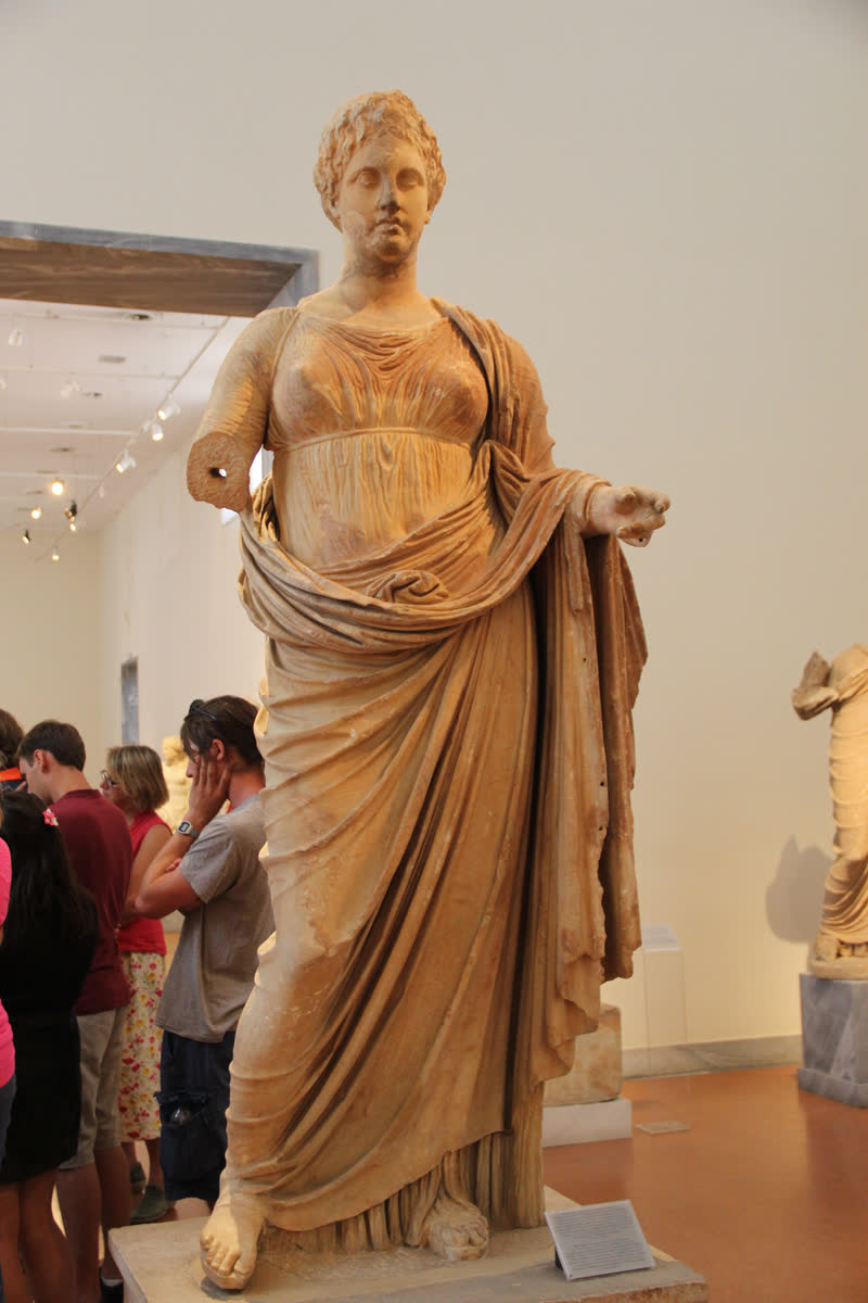 Têmis de pé, de quíton cingido e manto atravessado, a mão esquerda estendida — a estátua que Cairestrato esculpiu para o santuário de Nêmesis em Ramnunte. Mármore pentélico, ca. 300 a.C. Museu Arqueológico Nacional de Atenas (231).